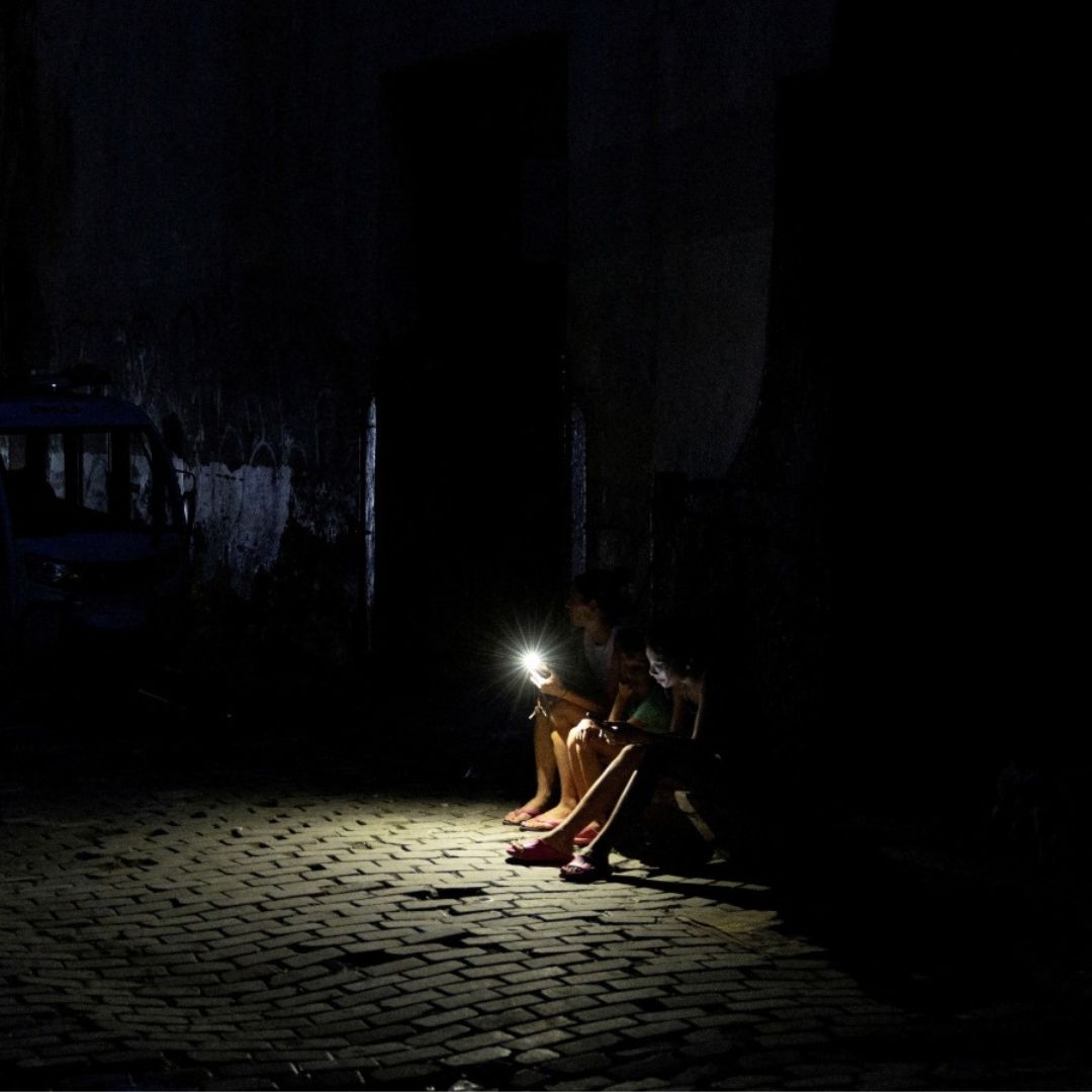 Varias personas se sientan en una calle oscura iluminada por la linterna de un teléfono móvil durante un apagón